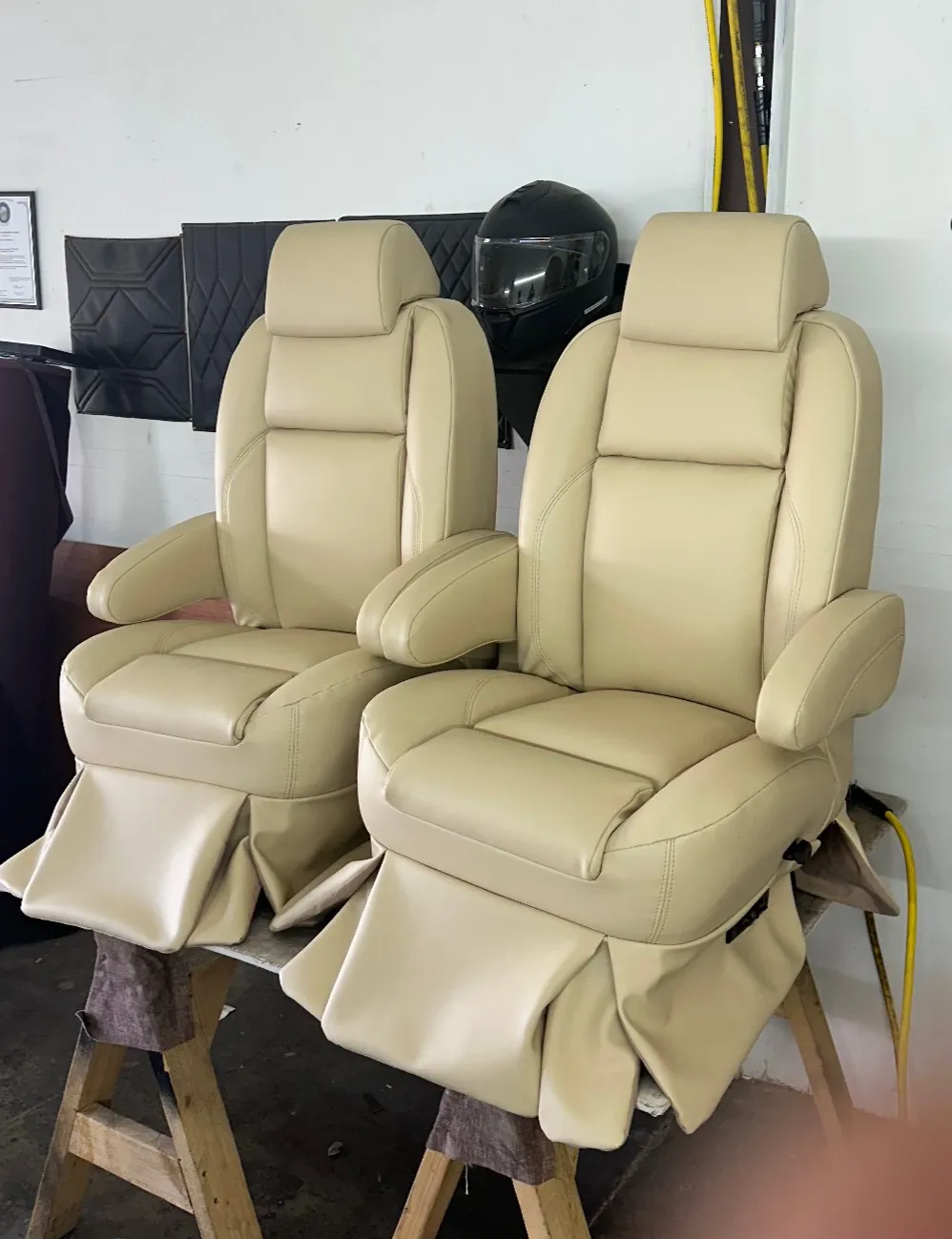 Pair of beige leather seats sitting atop a wooden stand in a garage