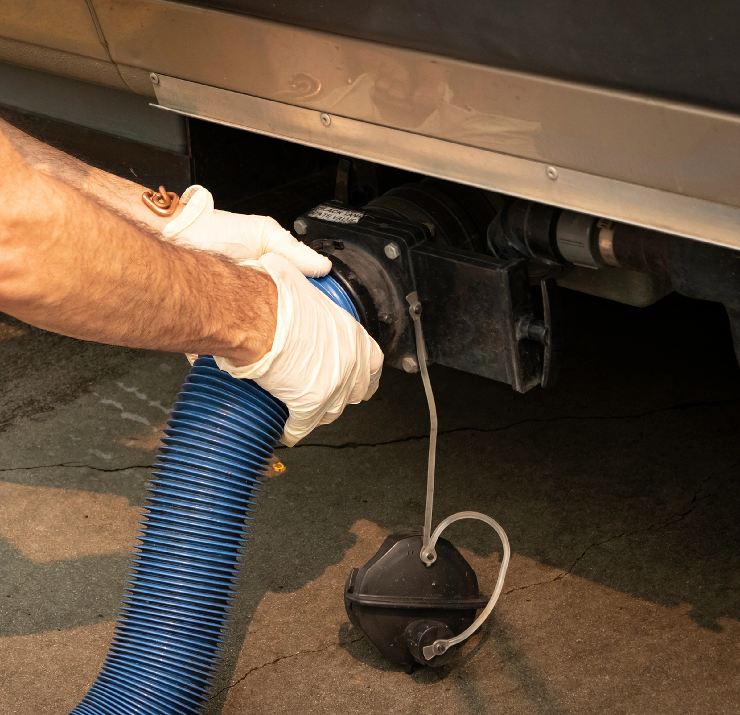 Man wearing white gloves holding a blue hose attached to the back of a truck