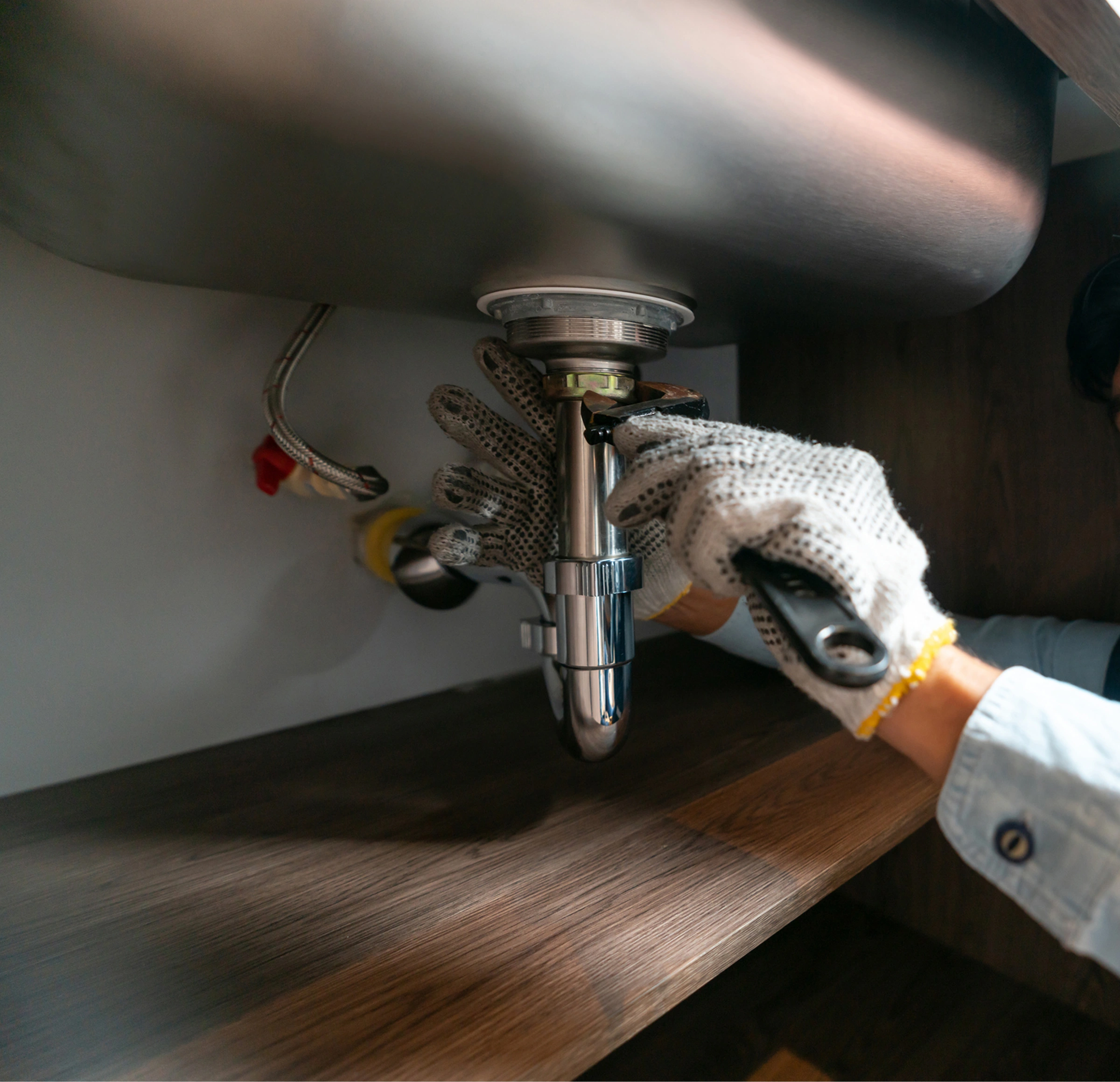 Plumber wearing gloves and working on a sink in a kitchen